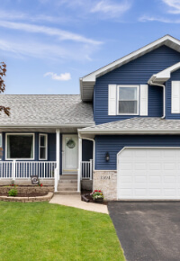 Exterior of a suburban home with blue siding, a white front porch, and white shutters.